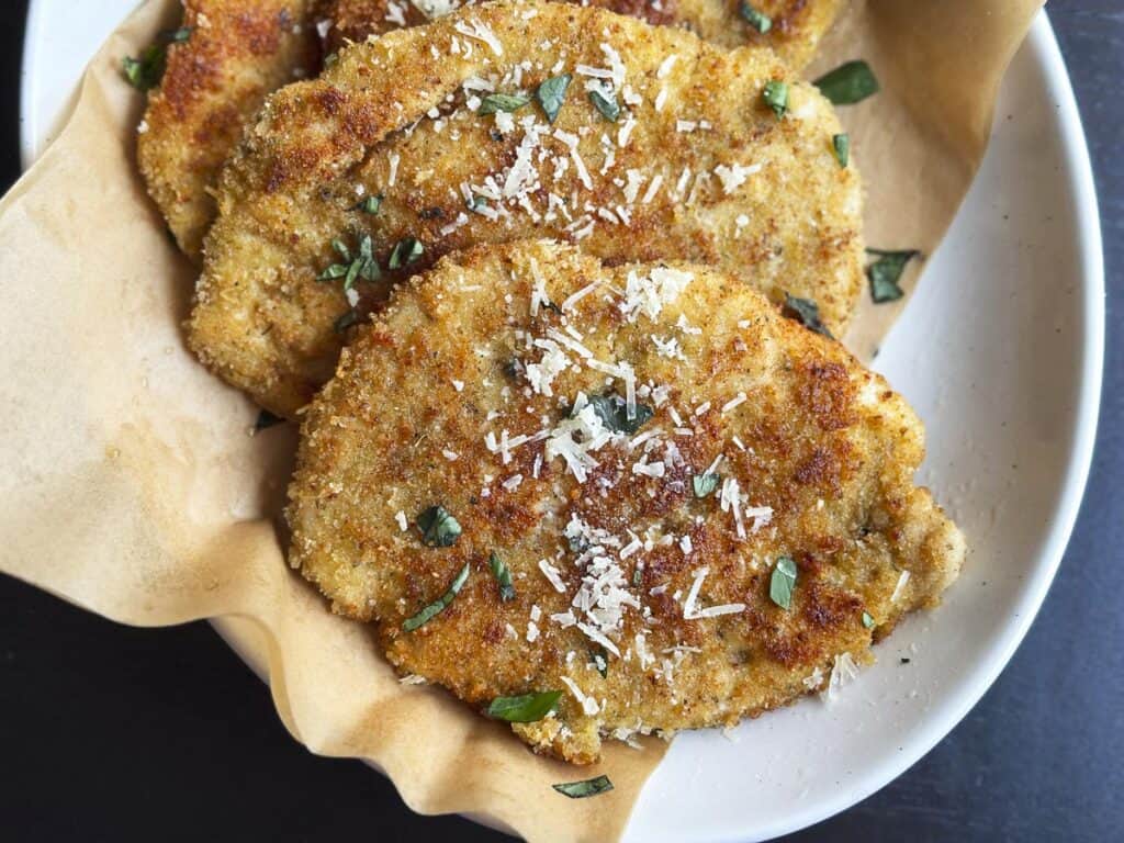 Three fried chicken cutlets on a white plate.