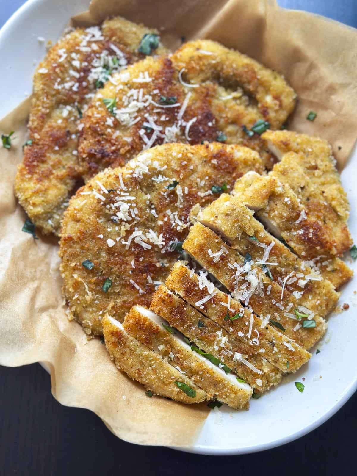 A plate of chicken cutlets with parmesan cheese sprinkled on top.