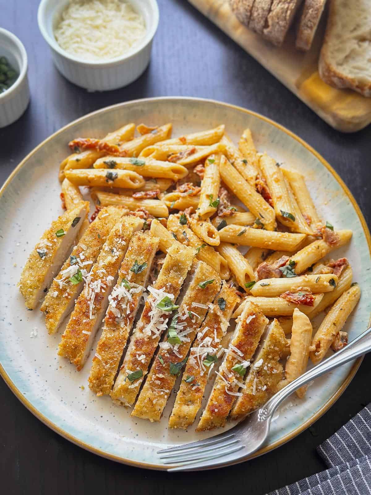 A sliced chicken cutlet with creamy sundried tomato pasta on a plate.