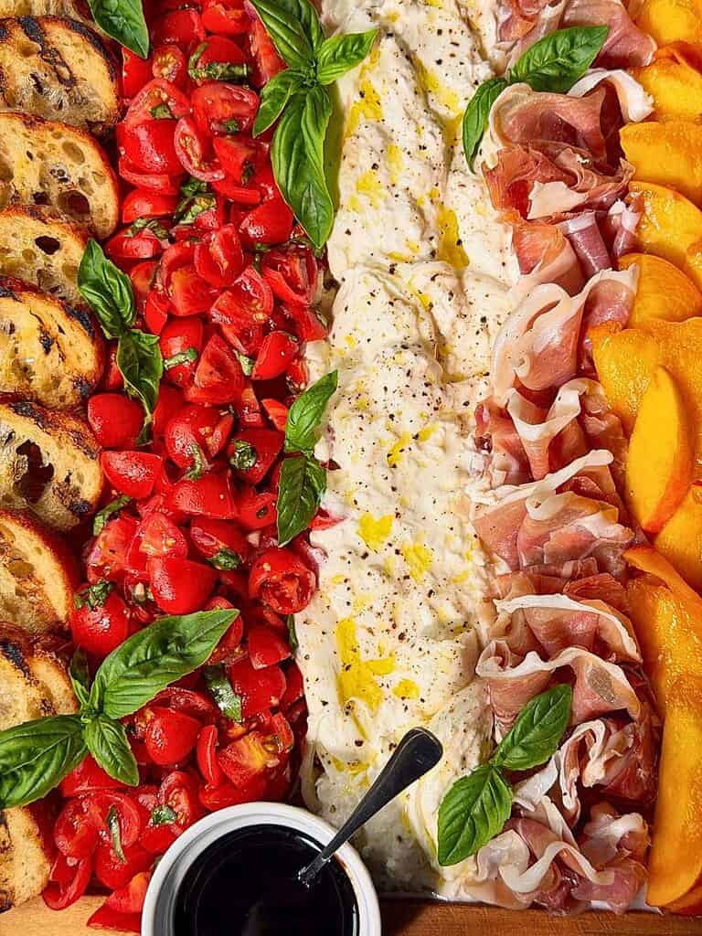 Grilled crostini, bruschetta tomatoes, balsamic glaze, torn burrata, prosciutto, basil crowns, and sliced peaches.