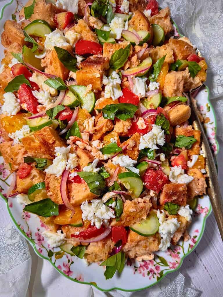 Colorful Panzanella bread salad with tomatoes, cucumbers, basil, and mozzarella cheese on a decorative plate.
