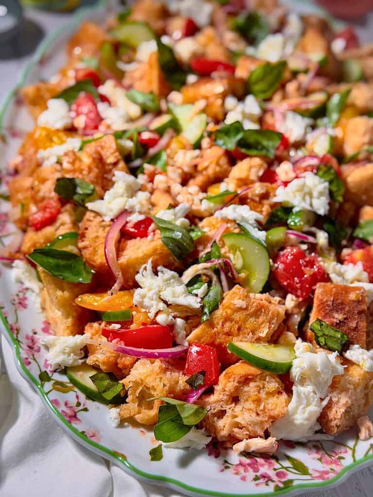 Panzanell salad with tomatoes, cucumber, mozzarella and fresh basil on a floral platter.