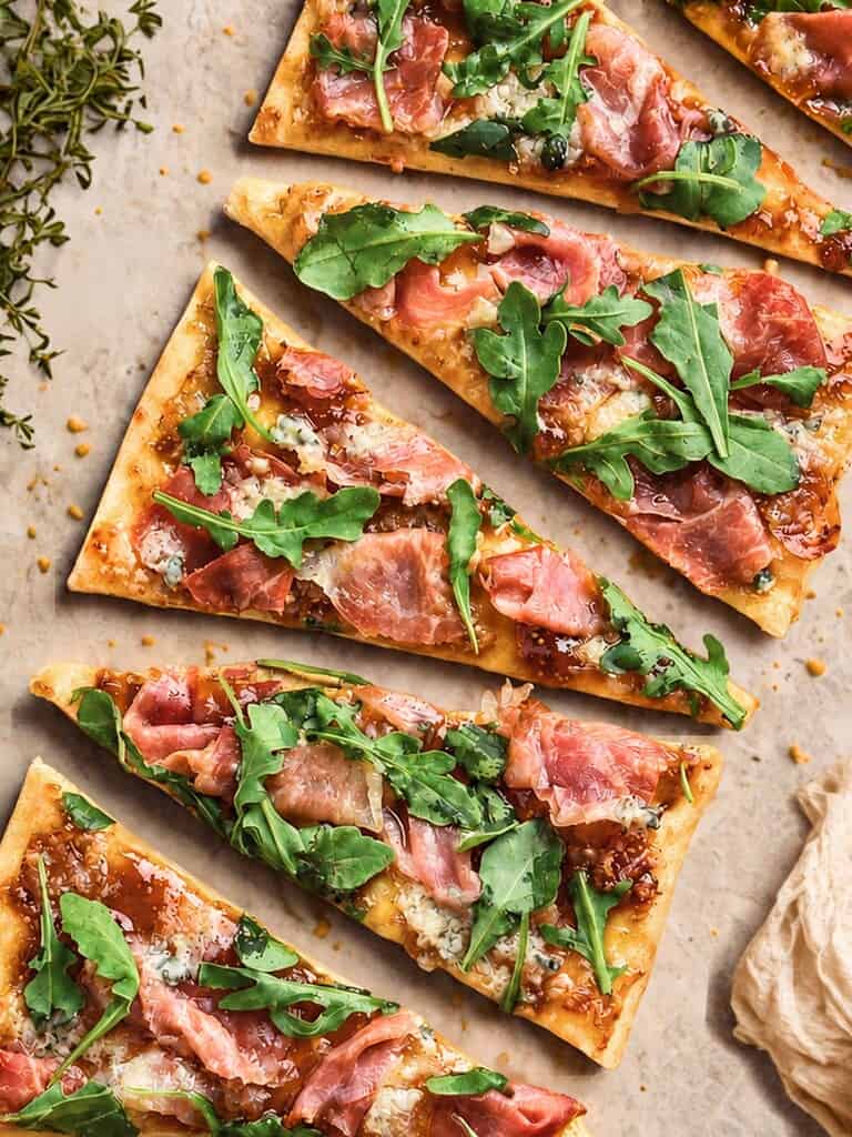 Gourmet flatbread pizza topped with prosciutto, arugula, and blue cheese, served on a rustic surface.