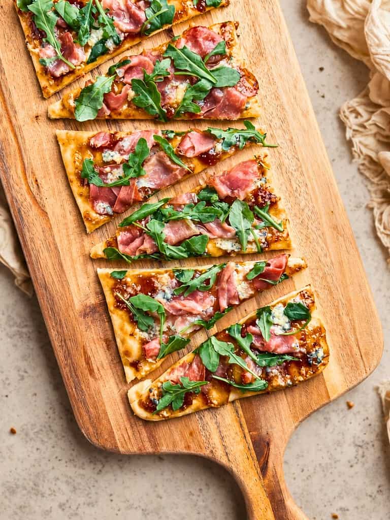 Delicious flatbread topped prosciutto, fig jam, and blue cheese on a wooden serving board.
