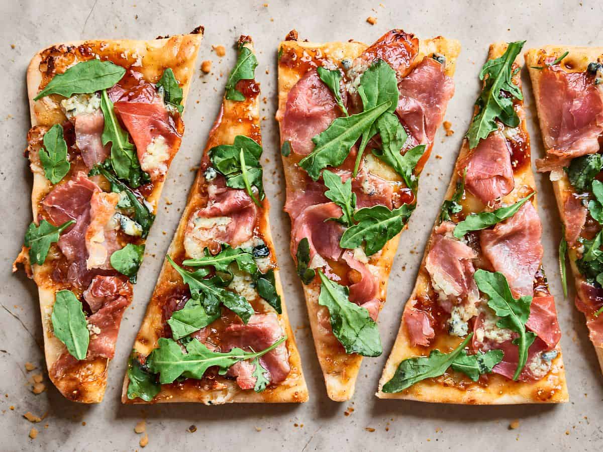 Prosciutto, fig jam, blue cheese, and fresh arugula on crispy flatbread, perfect for a quick gourmet snack or app.