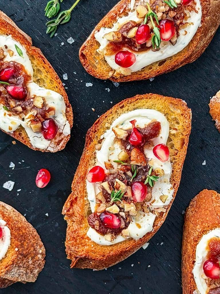 Close up of goat cheese crostini with pomegranate, pecans, apple butter, and fresh thyme.