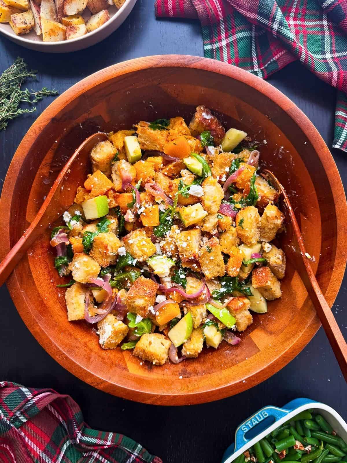 Fall panzanella salad with caramelized squash and red onion with green apple, arugula, and goat cheese in a large wooden salad bowl.