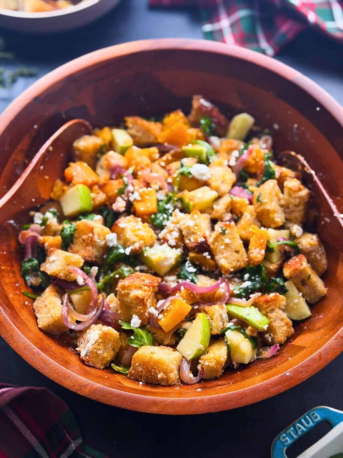 Fall panzanella salad with squash, apples, onions, arugula, and goat cheese in a large wooden bowl.