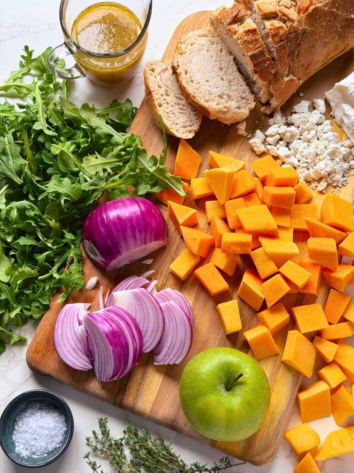 Cubed squash, red onion, green apple, sourdough bread, arugula, thyme, and goat cheese on a wooden board.