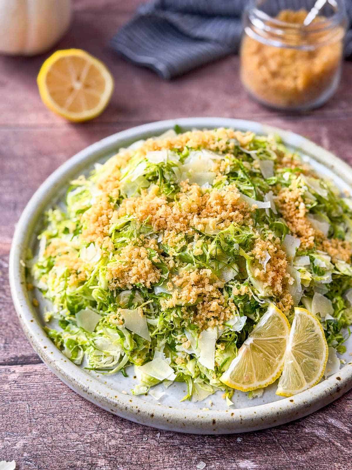 Shaved brussels sprouts salad with parmesan curls and garlic breadcrumbs on a round white speckled plate.