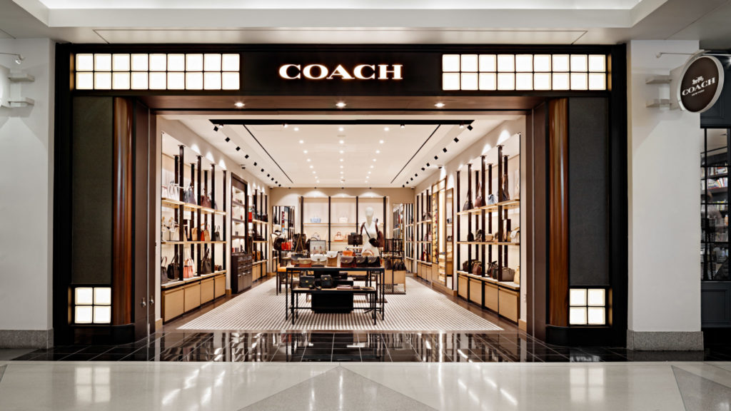 Coach store entrance with illuminated sign and luxury interior display.