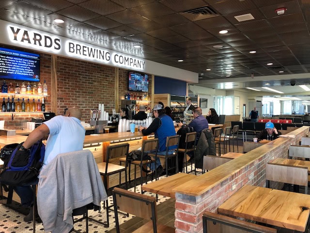 People sitting at the bar inside Yards Brewing Company with wooden tables and brick walls.
