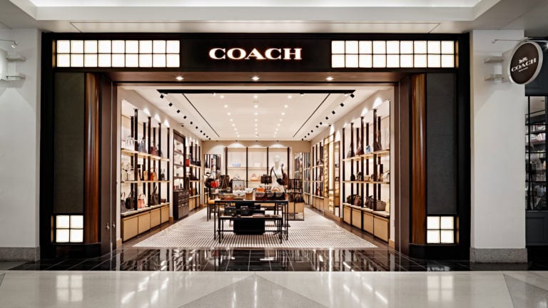 Coach store entrance with illuminated sign and luxury interior display.