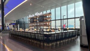 Modern airport bar with high stools and large windows overlooking the tarmac.