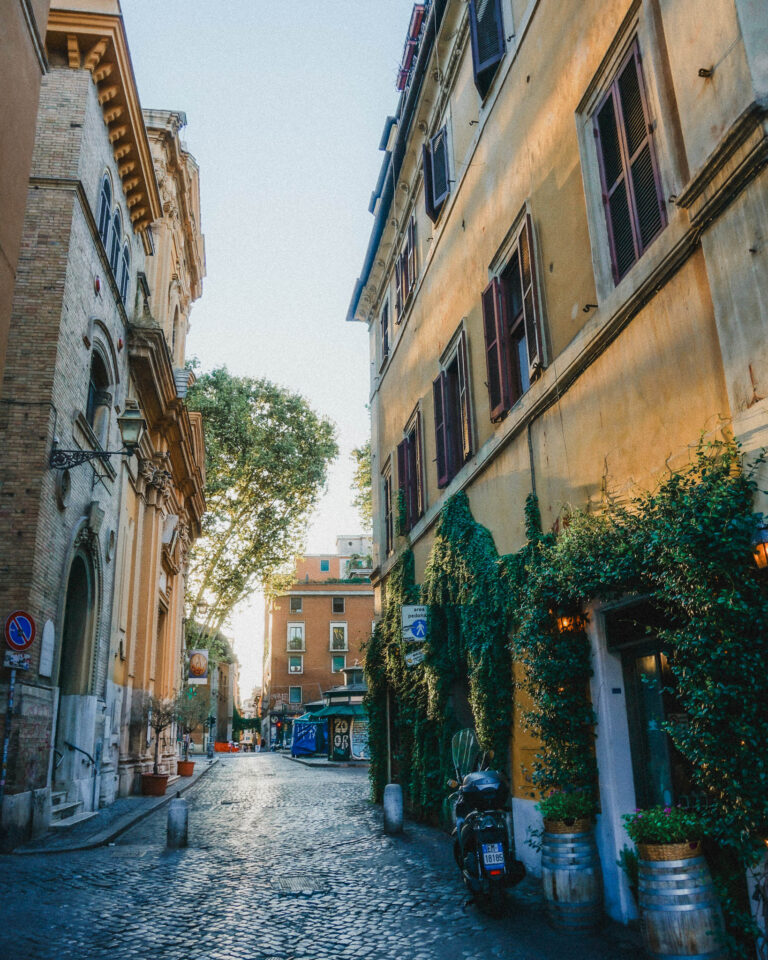 If you're staying in Rome for your first time, I recommend staying in this beautiful neighborhood called Trastevere. You can see that this area has plenty of cobblestone streets and narrow streets that open up into beautiful piazzas or churches. You'll often find mopeds parked along the ancient facades and luscious vegetation scaling and climbing these Roman buildings.