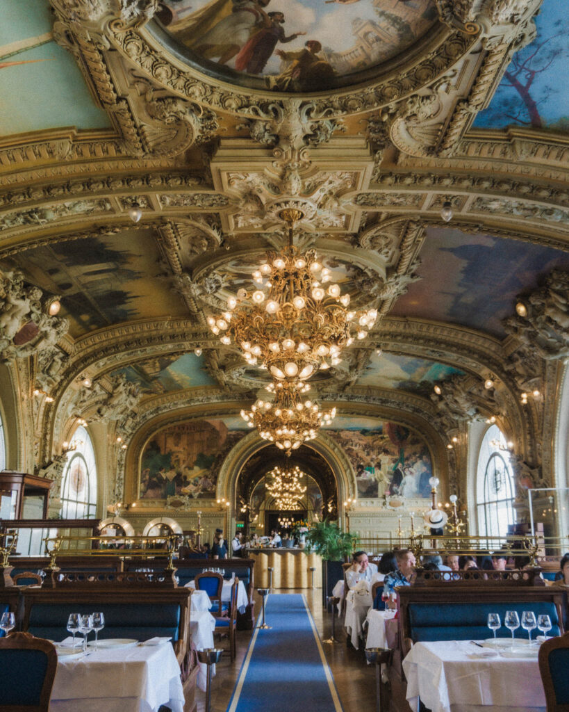 Paris is one of the most beautiful cities in the world, and for good reason! Here's one of the best restaurants in Paris, Le Train Bleu! The inside decor is simply stunning, in a Parisian Rococo aesthetic the ceiling is a mix of lovely paintings and ornate gold carvings and statues. There are a few massive crystal chandeliers hanging, and the walkways are paved with blue runners that match the satin blue seating. Some of the seating is old school booths, in an art deco style.