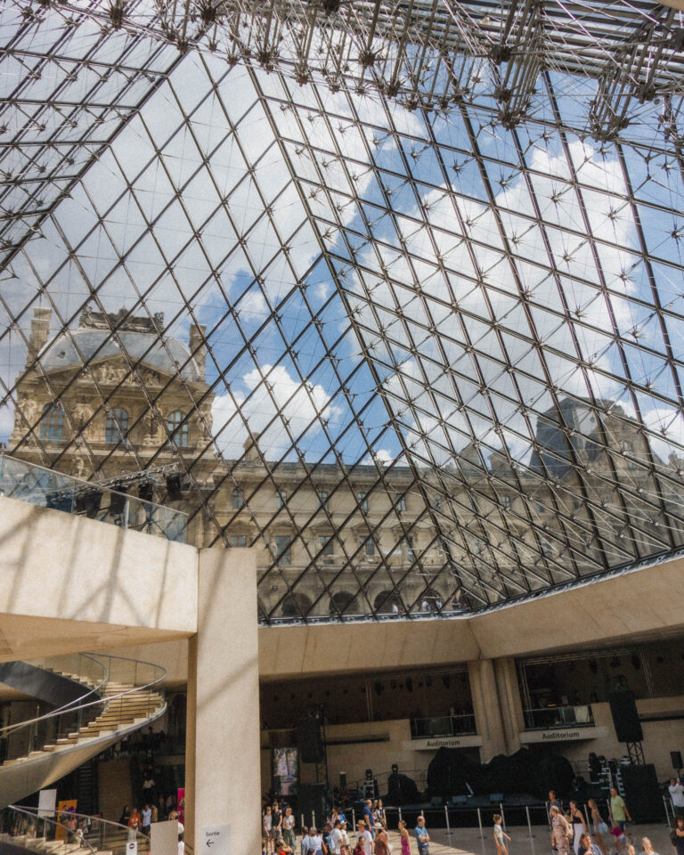 Here is the most dramatic museum entrance, the entrance to the Louvre when you're taking the escalator under the massive glass pyramid. Since the glass pyramid roof is glass, you can see the surrounding part of the museum outside with it's traditional Parisian decor, the building in a cream, stone color with a gray roof. The massive atrium that the escalator takes you down into has a cafe and different areas to enter the museum through.