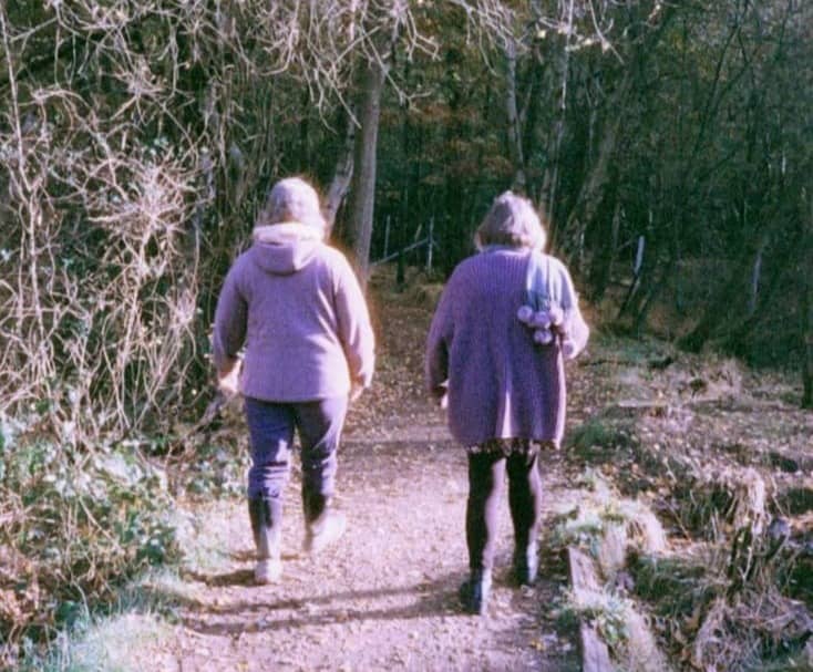 Two people walking on a path through woods.