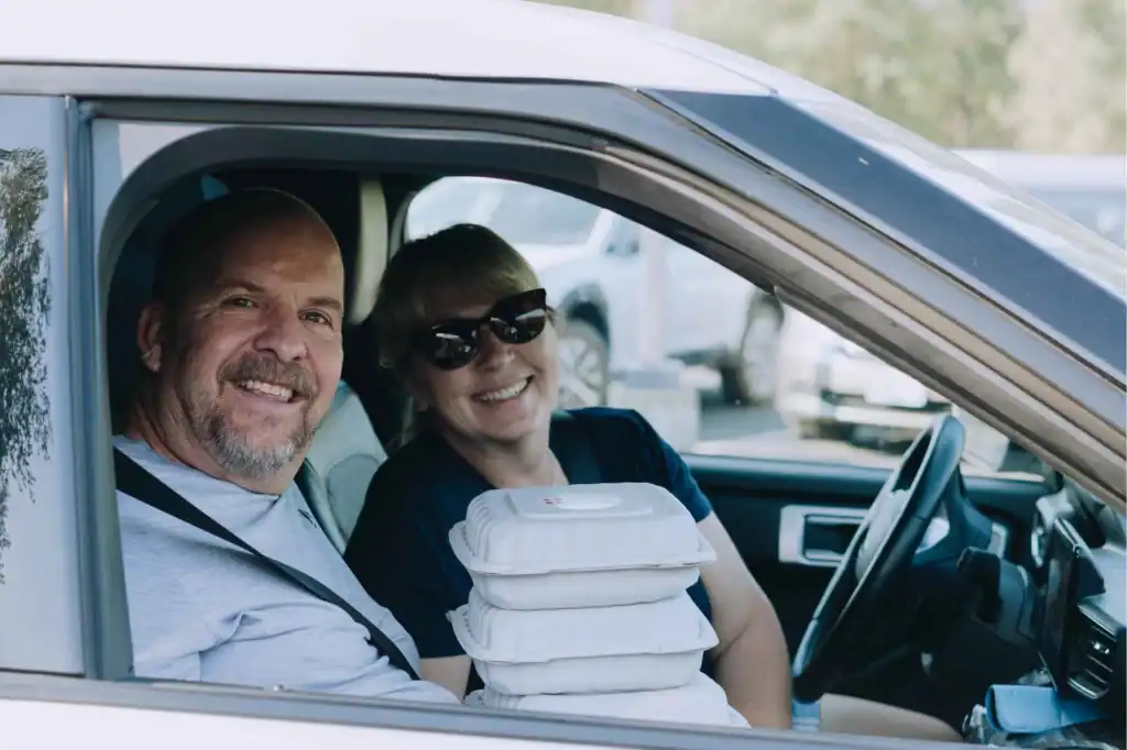 Woman in driver's seat and man in passanger holding three Mercy Chefs meals, Nine Mile Falls, Washington