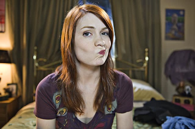 Red-haired woman with playful expression in a cozy bedroom.