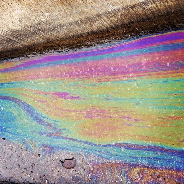 Colorful oil slick on concrete with rainbow hues and textured surface.