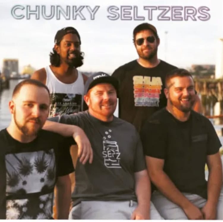 Group of five men outdoors with a city skyline in the background.