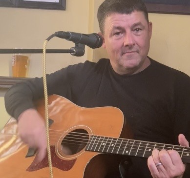 Man playing acoustic guitar and singing into a microphone at Michael's Harborside.