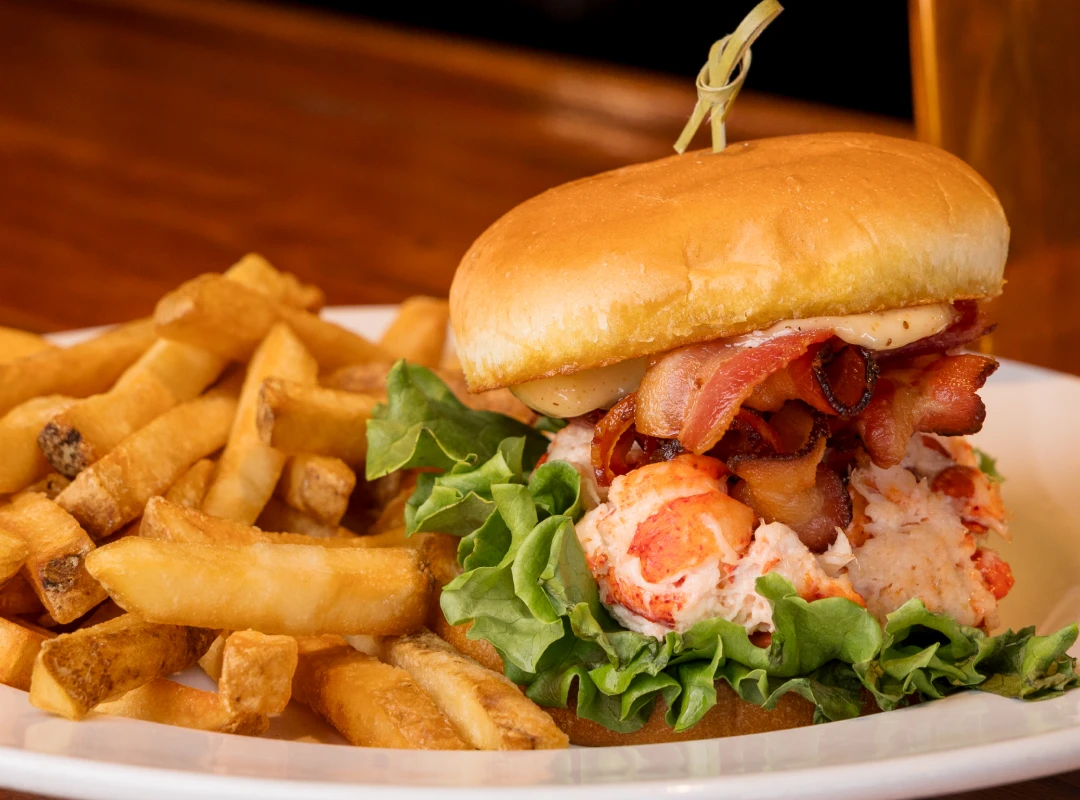 Lobster roll with bacon and lettuce, served with fries on a white plate.