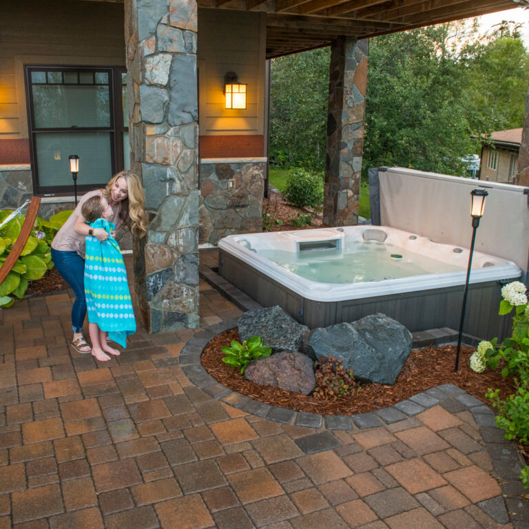 Hot tub with cover on a brick patio in a backyard setting.
