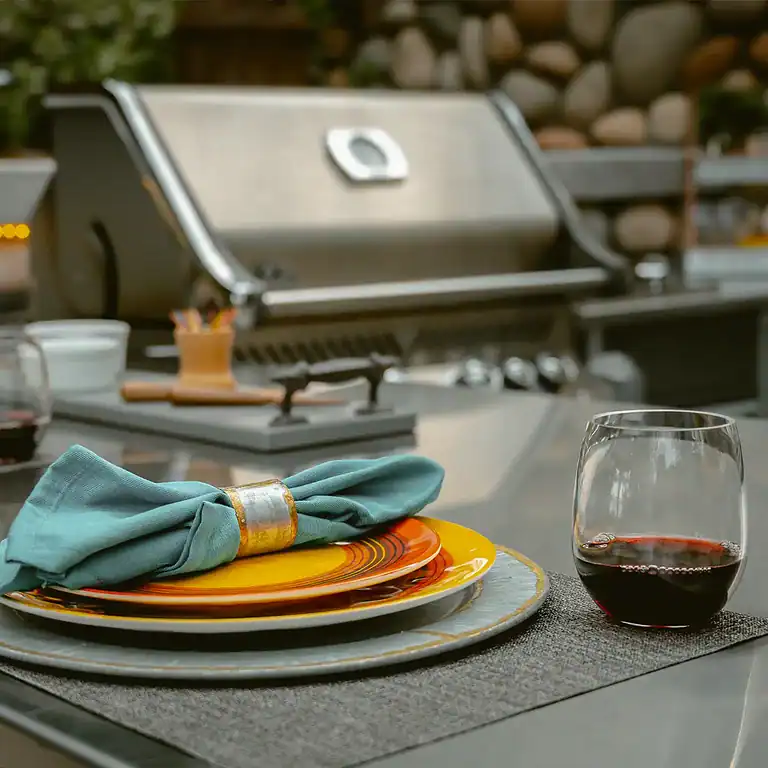 Outdoor kitchen with grill, plates, napkin, and glass of wine.