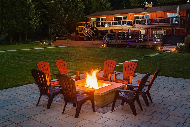 Firepit with glowing flames surrounded by chairs in a backyard setting.