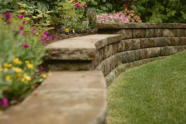 Retaining wall made of natural stone with vibrant flowers and well-maintained grass.