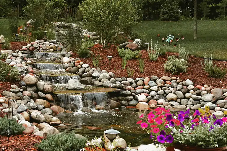 Water feature with rocks and plants in a landscaped yard.