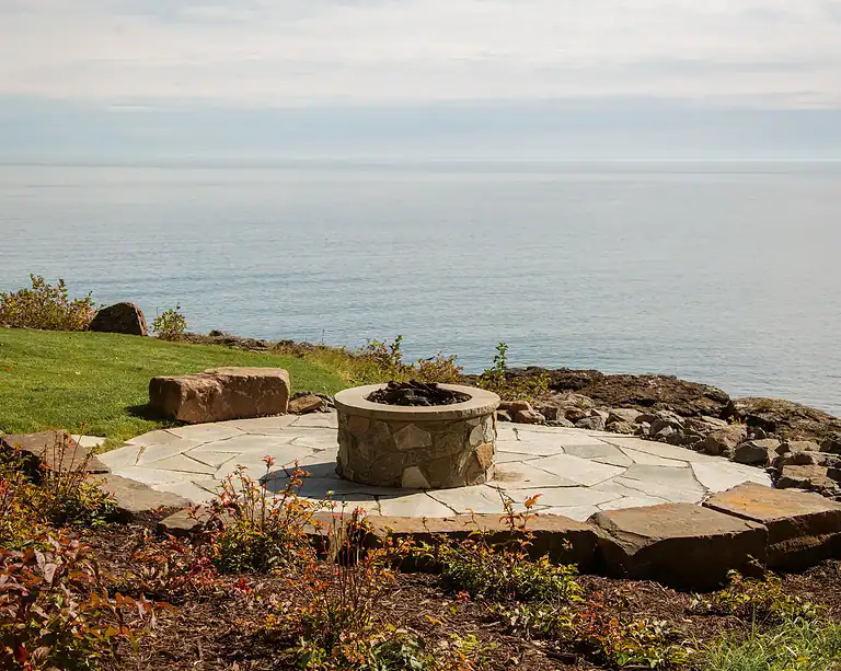 Outdoor fire pit on a stone patio with a lake view and natural landscape. Perfect for relaxing eveni.