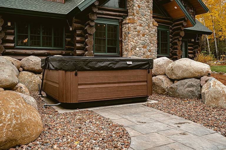 Hot tub placed outdoors near a rustic log cabin with stone accents.