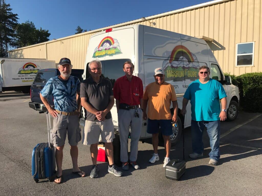 Four men standing in front of a van with luggage.
