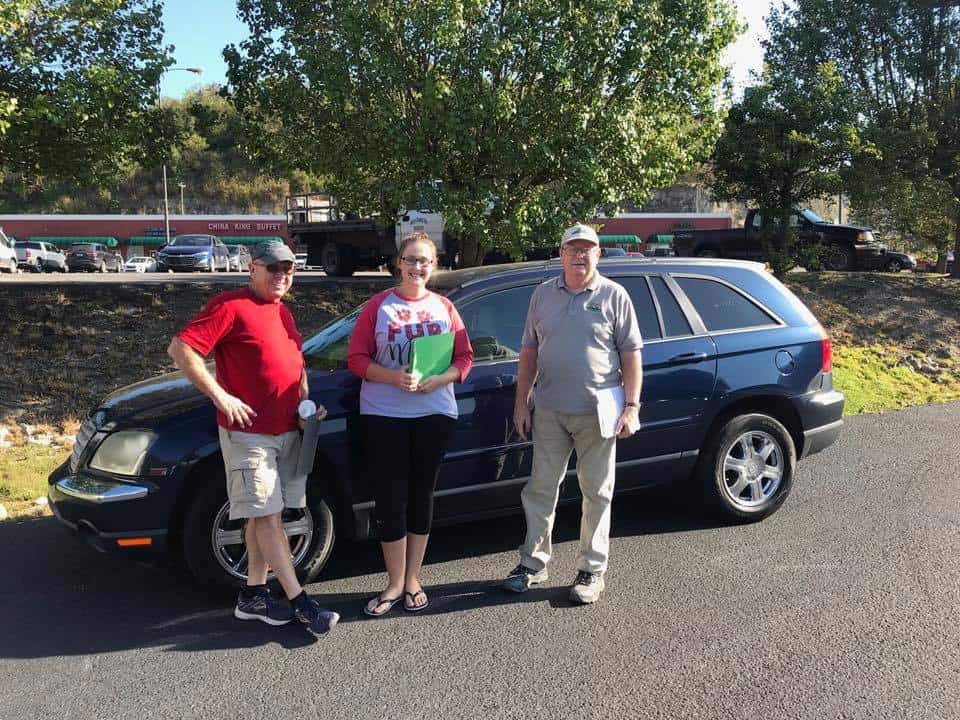 Three people standing in front of a blue car.