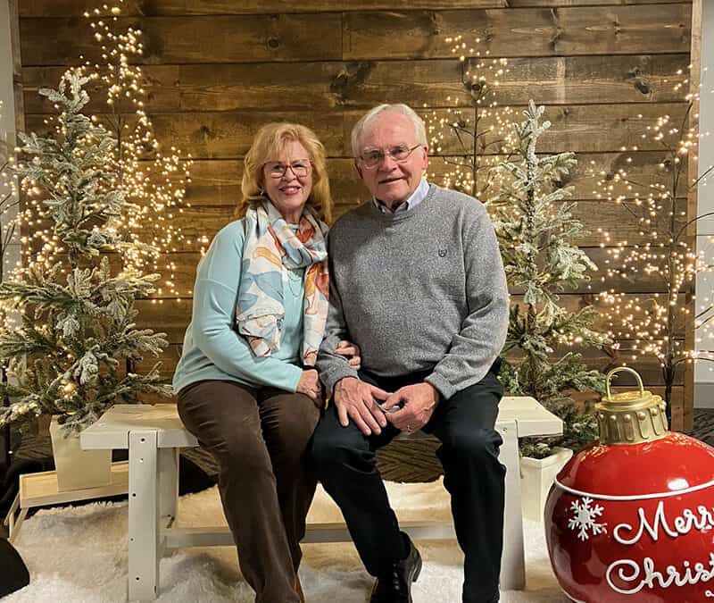A couple sitting on a bench in front of a christmas tree.