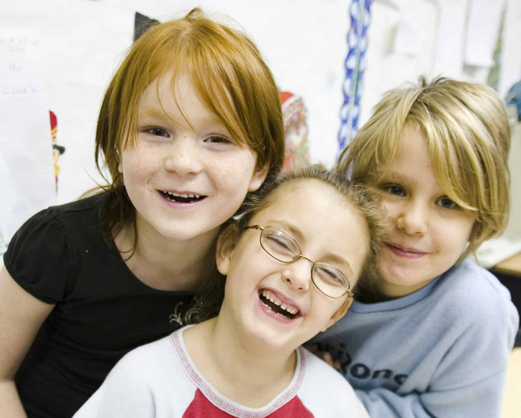 Three children posing for a photo in a classroom. Enjoying life thanks to mission of hope donations.