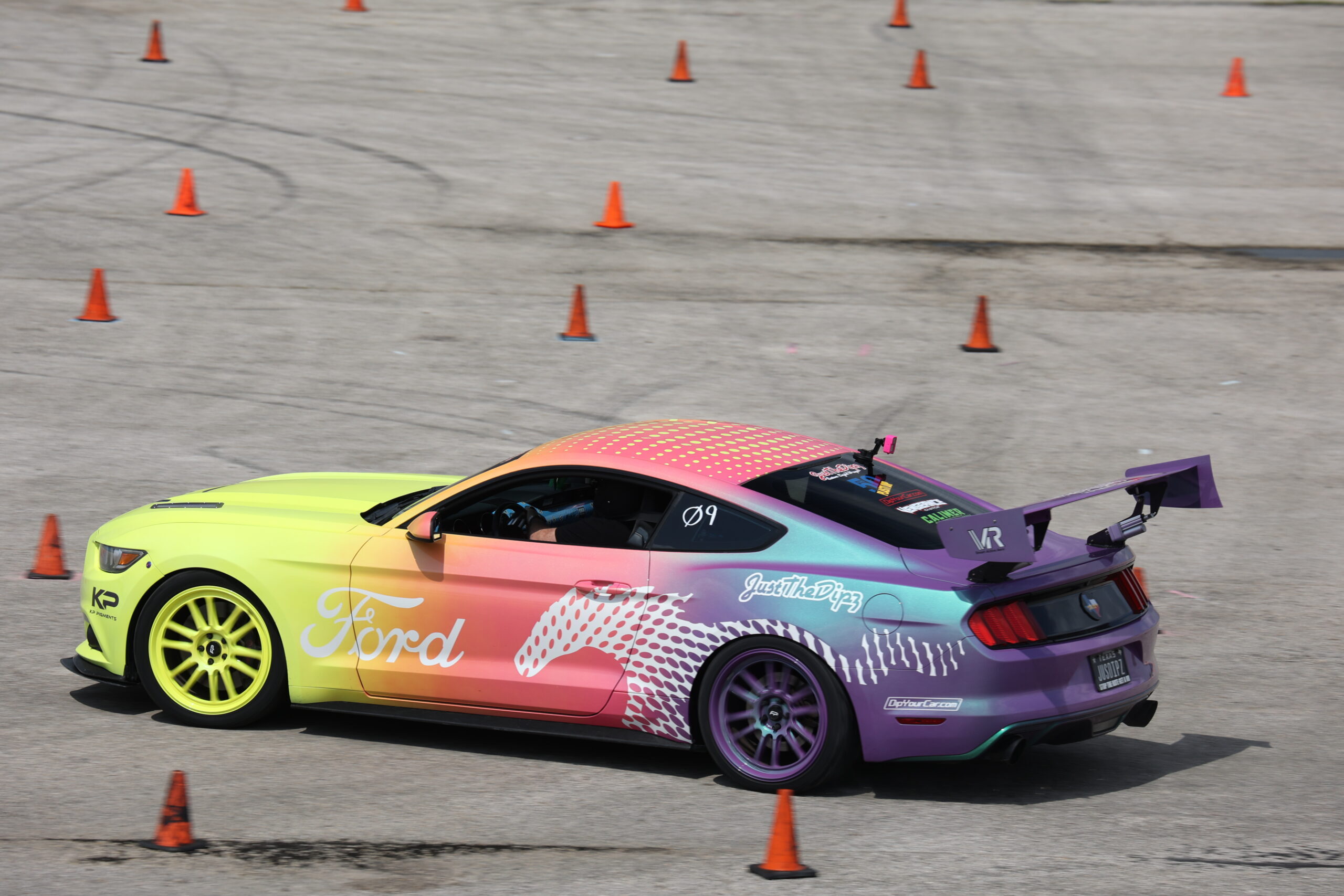 Colorful Ford Mustang drifting through cones at Mustang Week event.