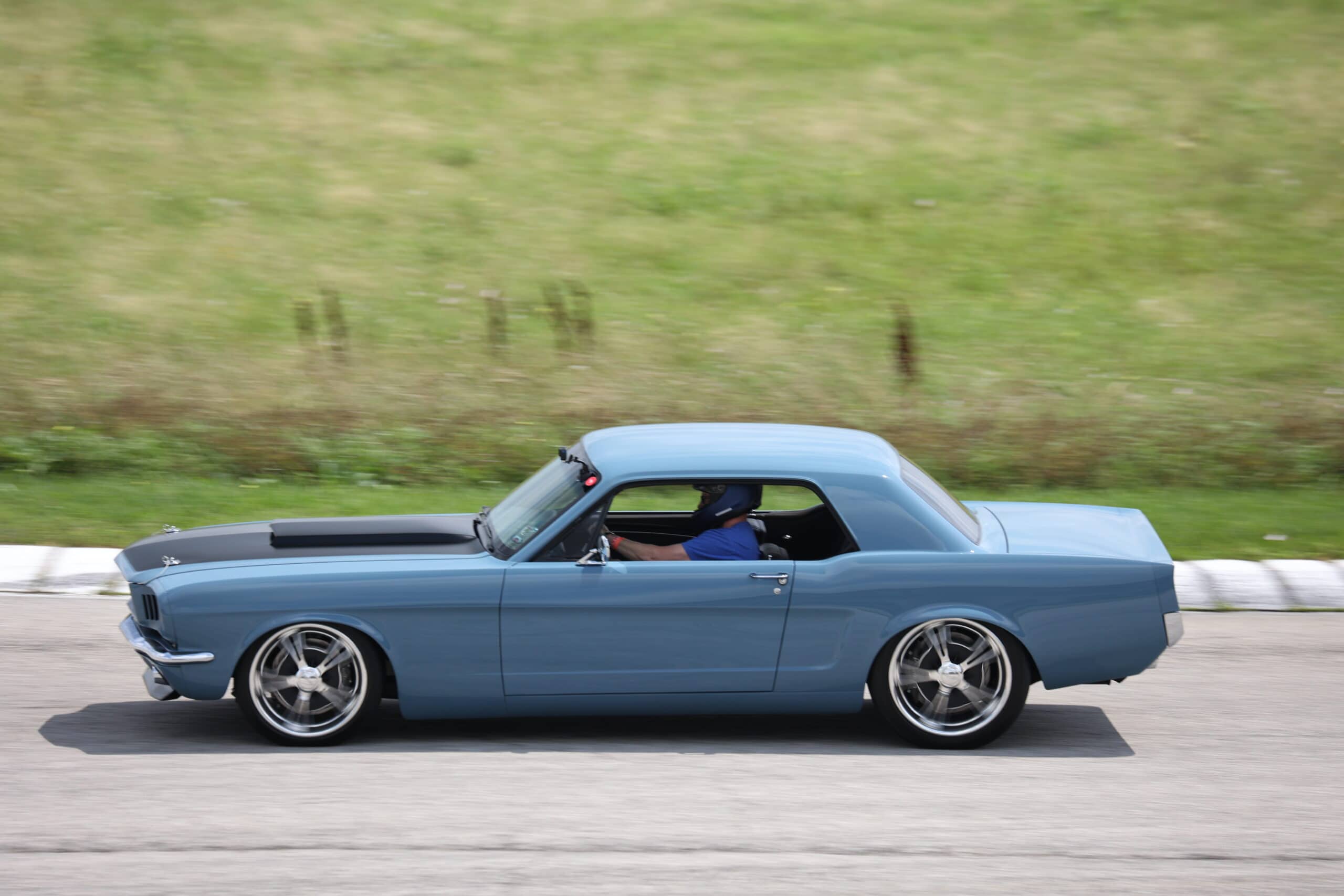 Blue vintage Ford Mustang driving on the road during Mustang Week event.