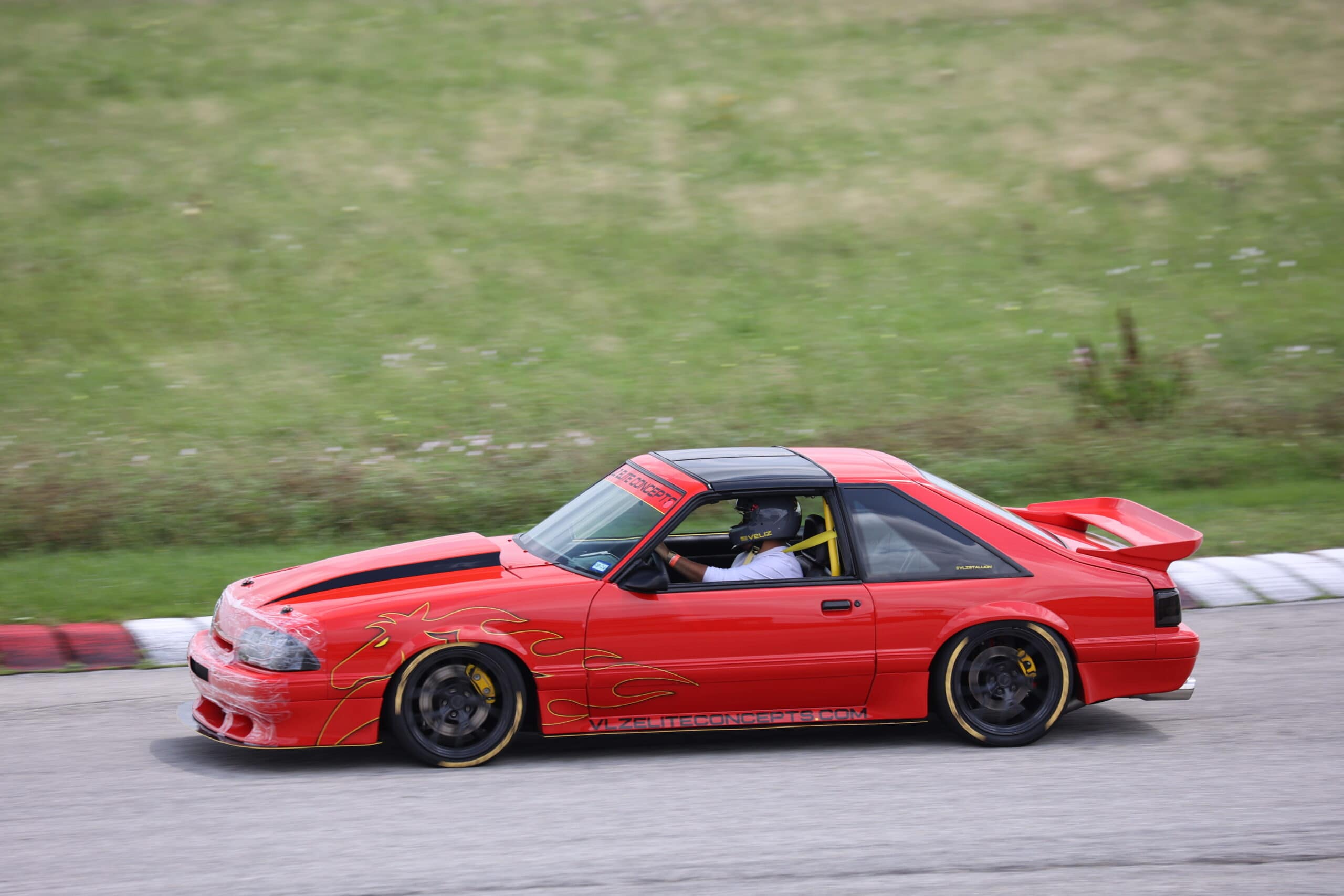 Red Mustang race car on track during Mustang Week event.