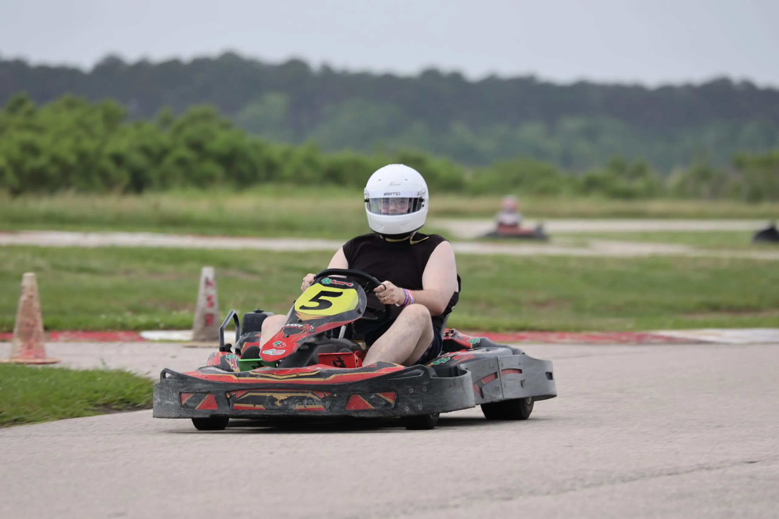 Person in helmet driving go-kart on race track during Mustang Week event.