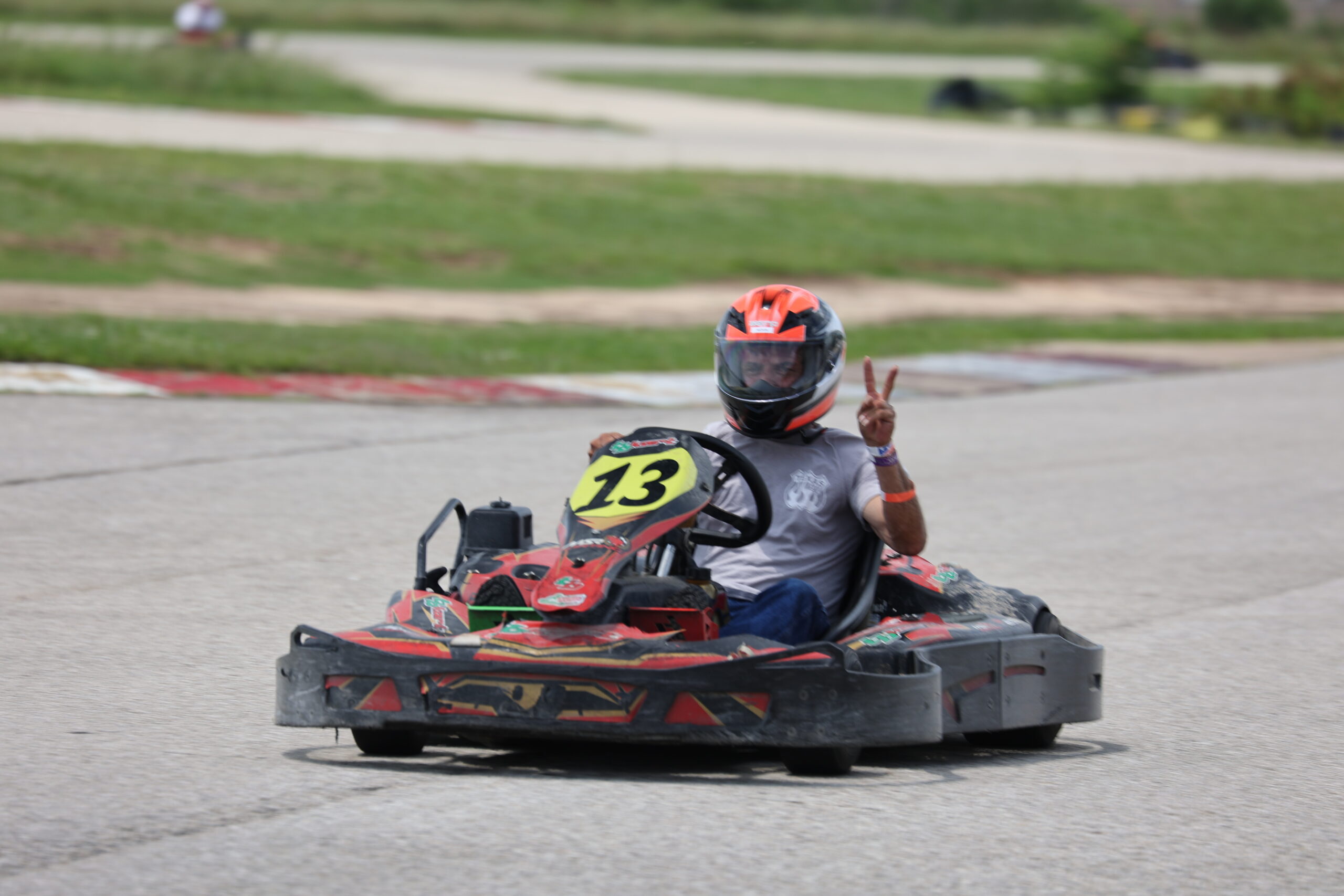 Go-kart driver wearing helmet making peace sign at Mustang Week event.