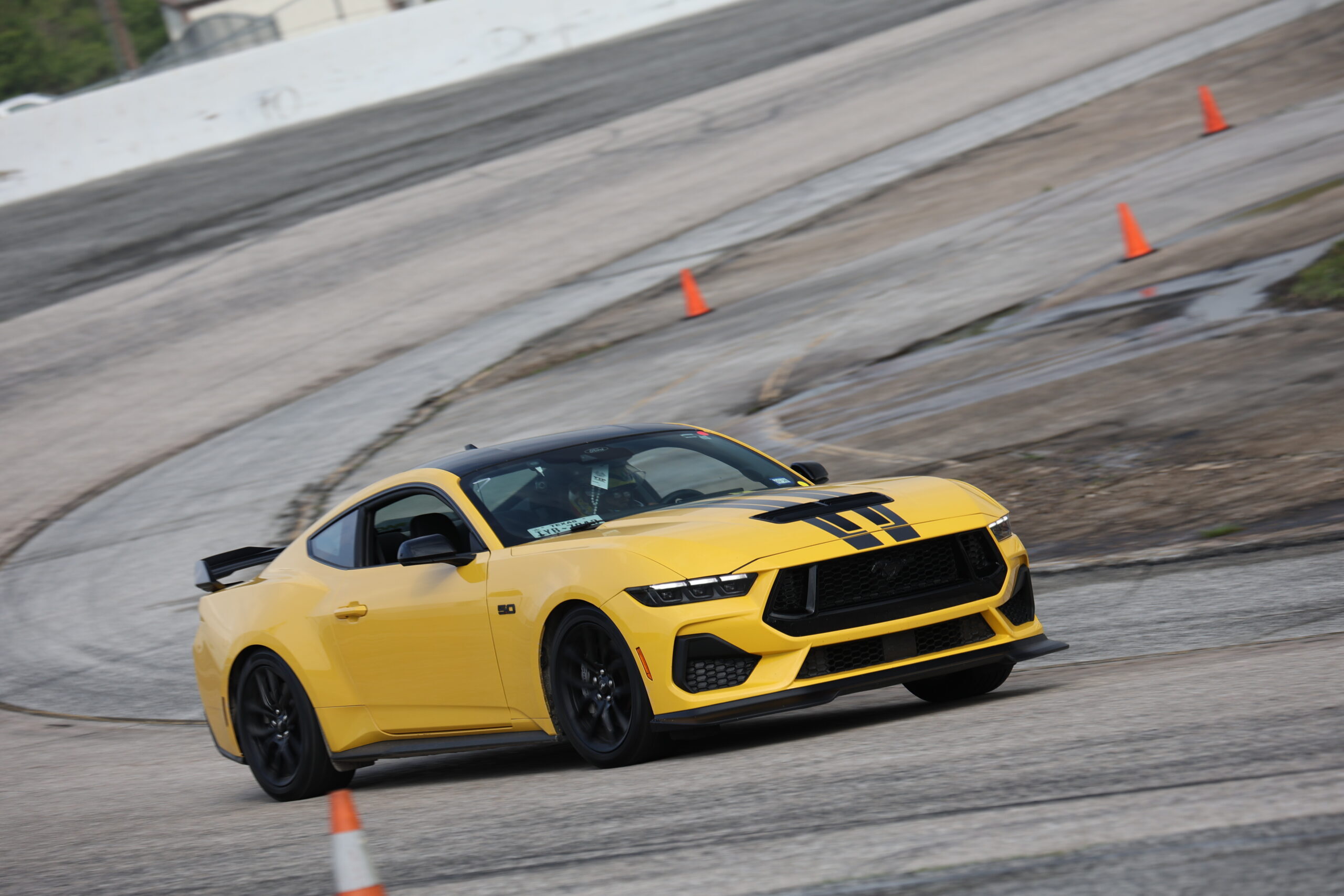 Yellow Ford Mustang racing on track at Mustang Week event.