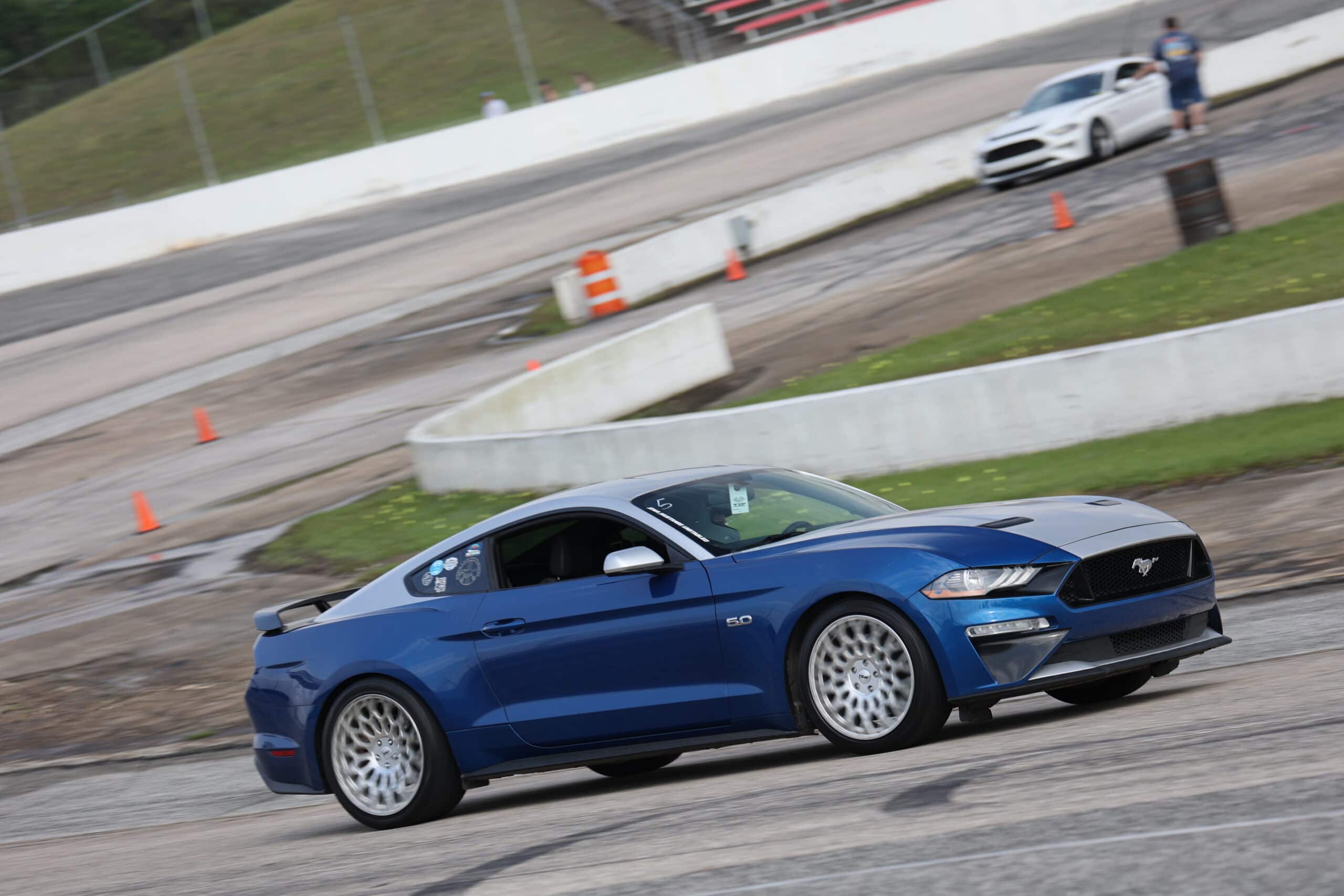 Blue Ford Mustang racing on track during Mustang Week event.