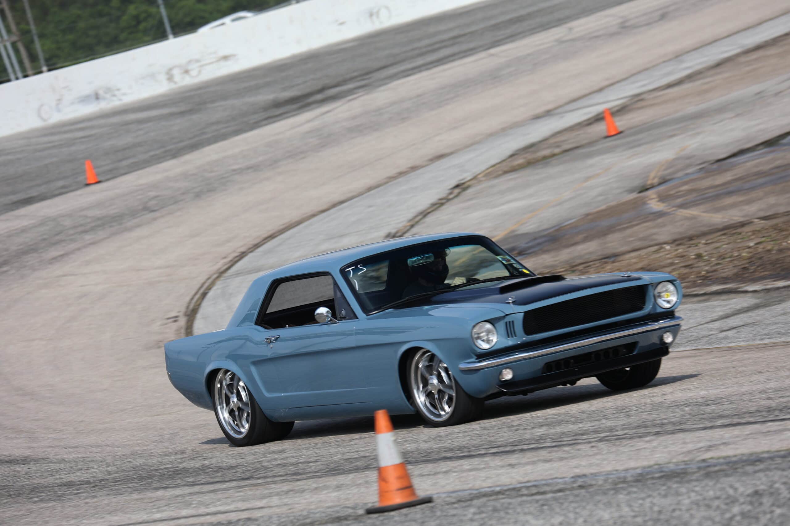 Blue vintage Ford Mustang racing on a track with orange cones.