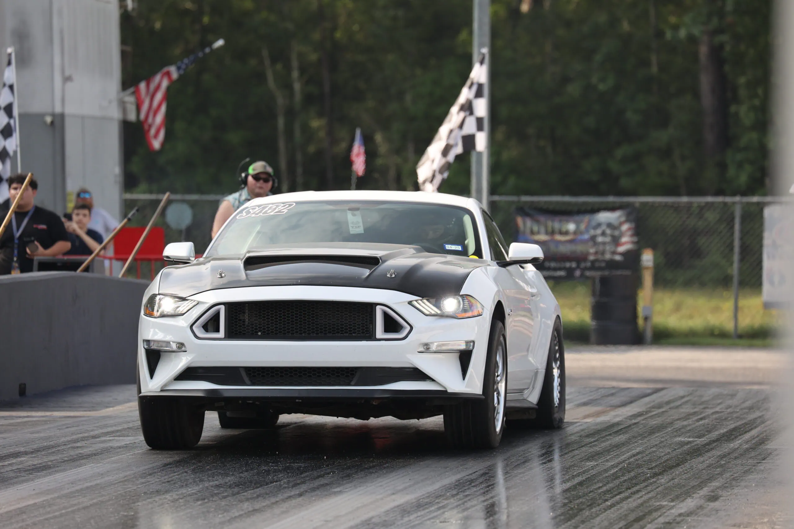 White Ford Mustang drag racing on track at Mustang Week event.