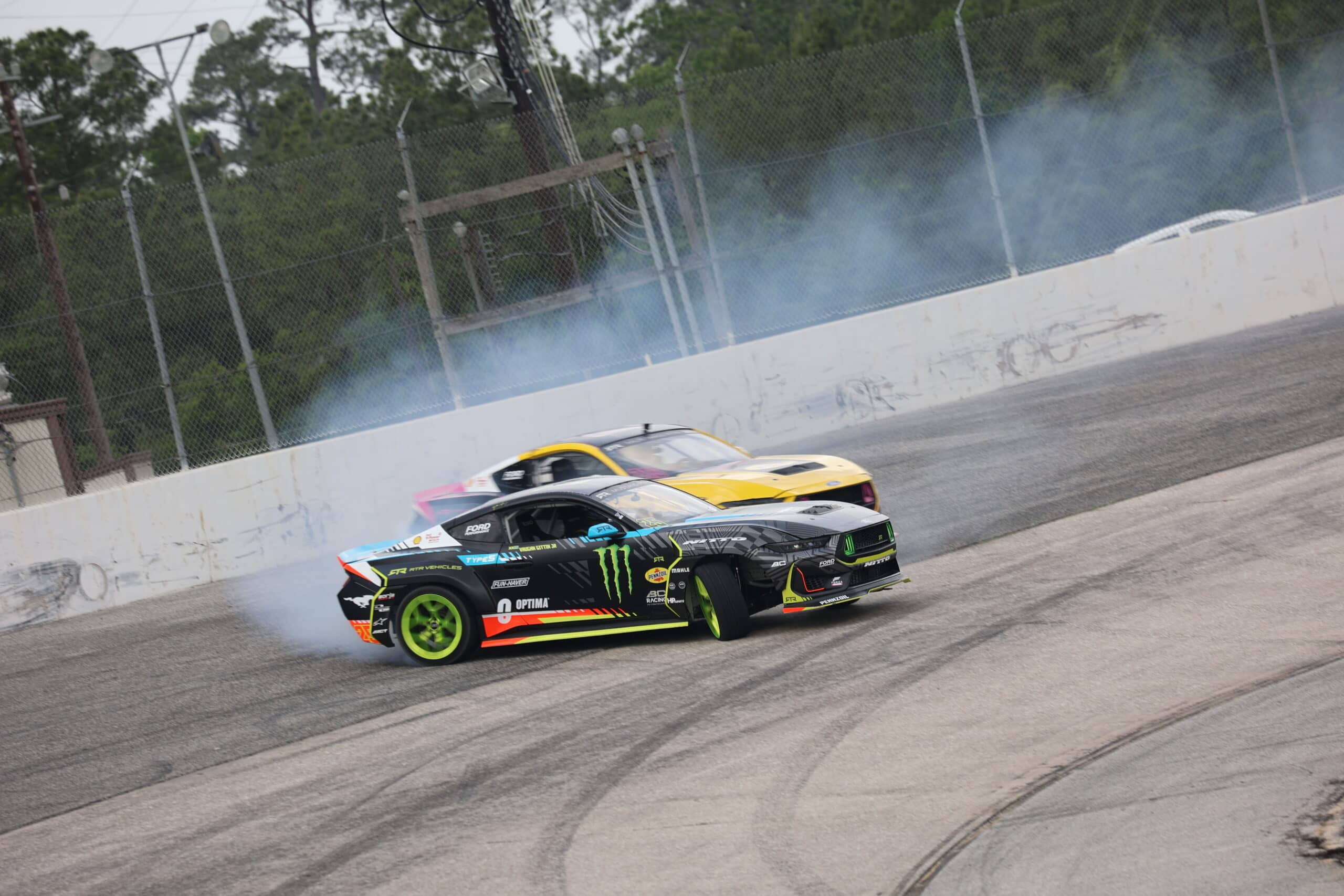 Two race cars drifting on the track during Mustang Week event.