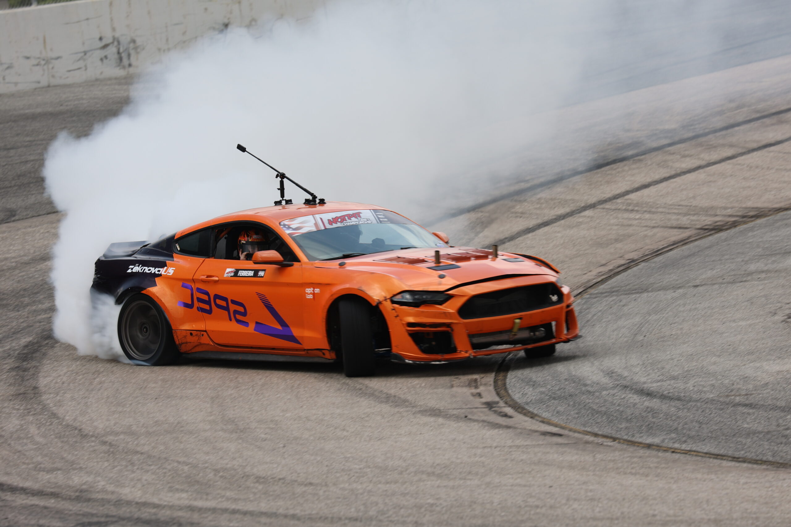 Orange drift car performing a burnout at Mustang Week event.